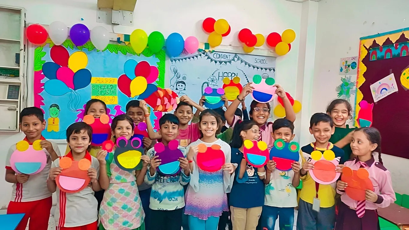Group of happy school children holding colorful handmade crafts in a decorated classroom with balloons and drawings on the walls.